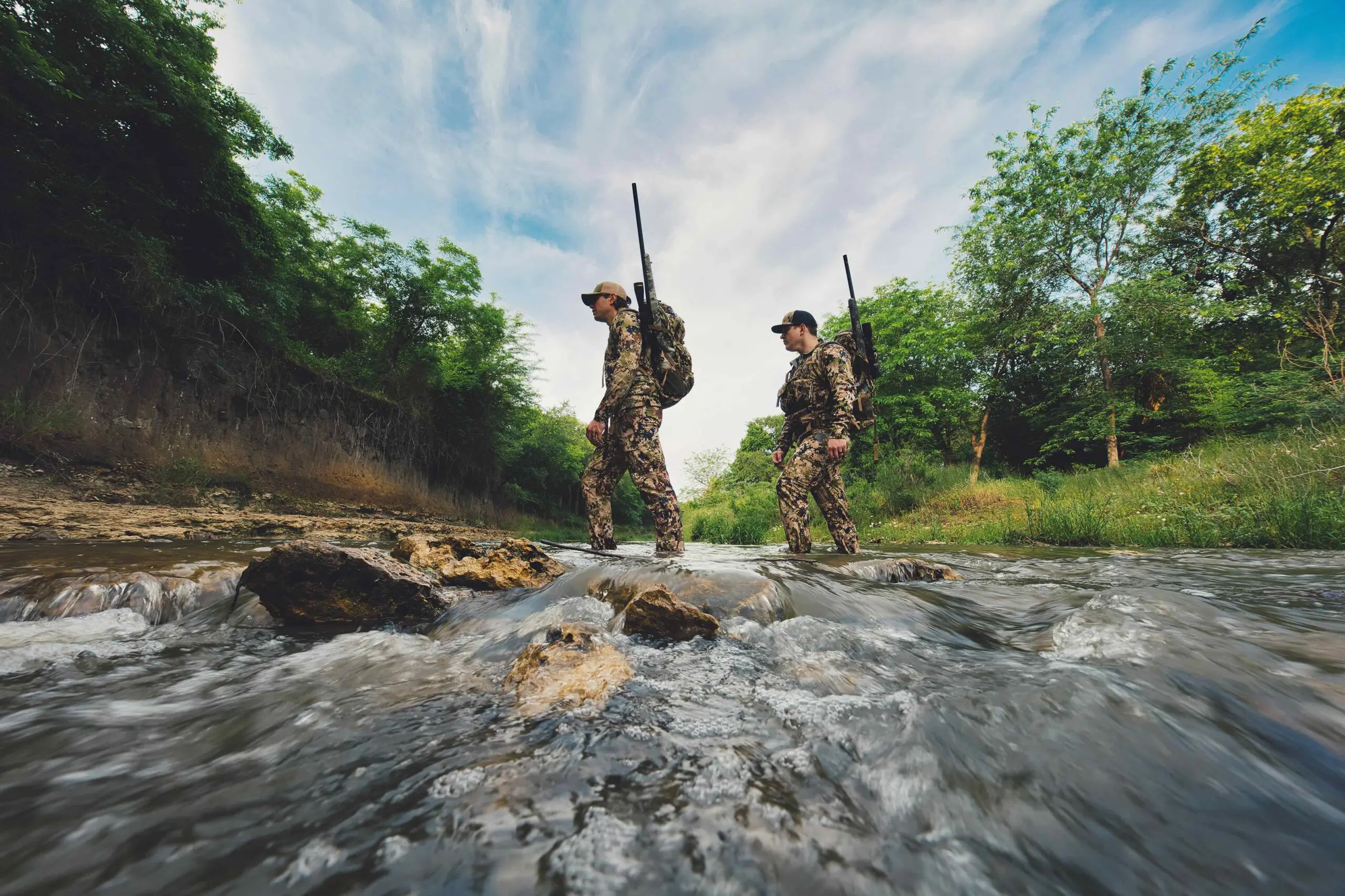 Hunters carrying rifles while crossing a creek