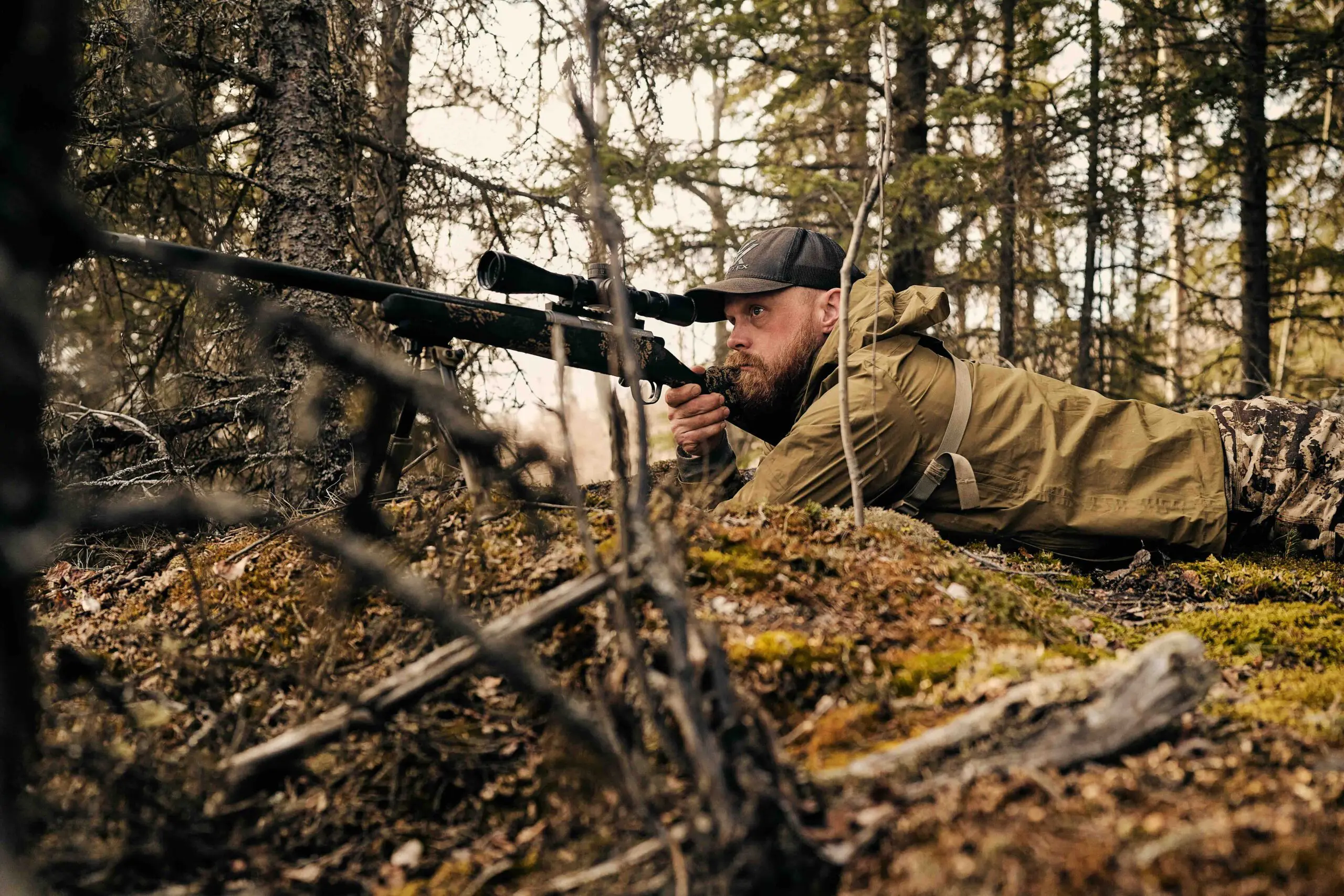 Hunter aiming a scoped Christensen Arms rifle from a field position
