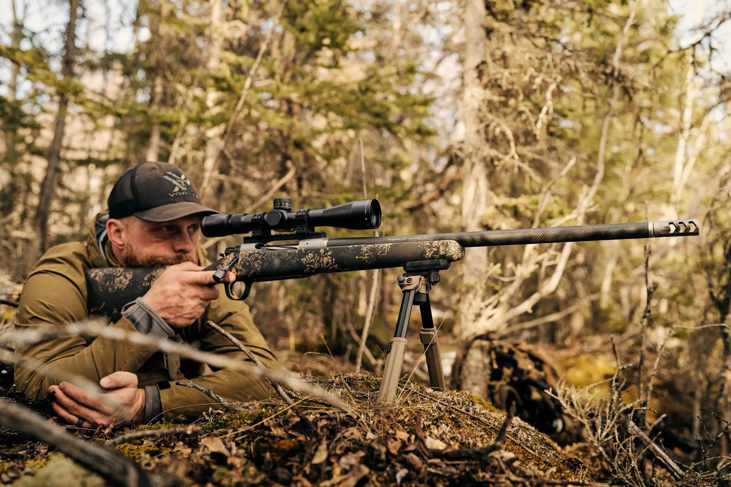 Hunter behind a scoped Christensen Arms rifle supported on a tripod in the field