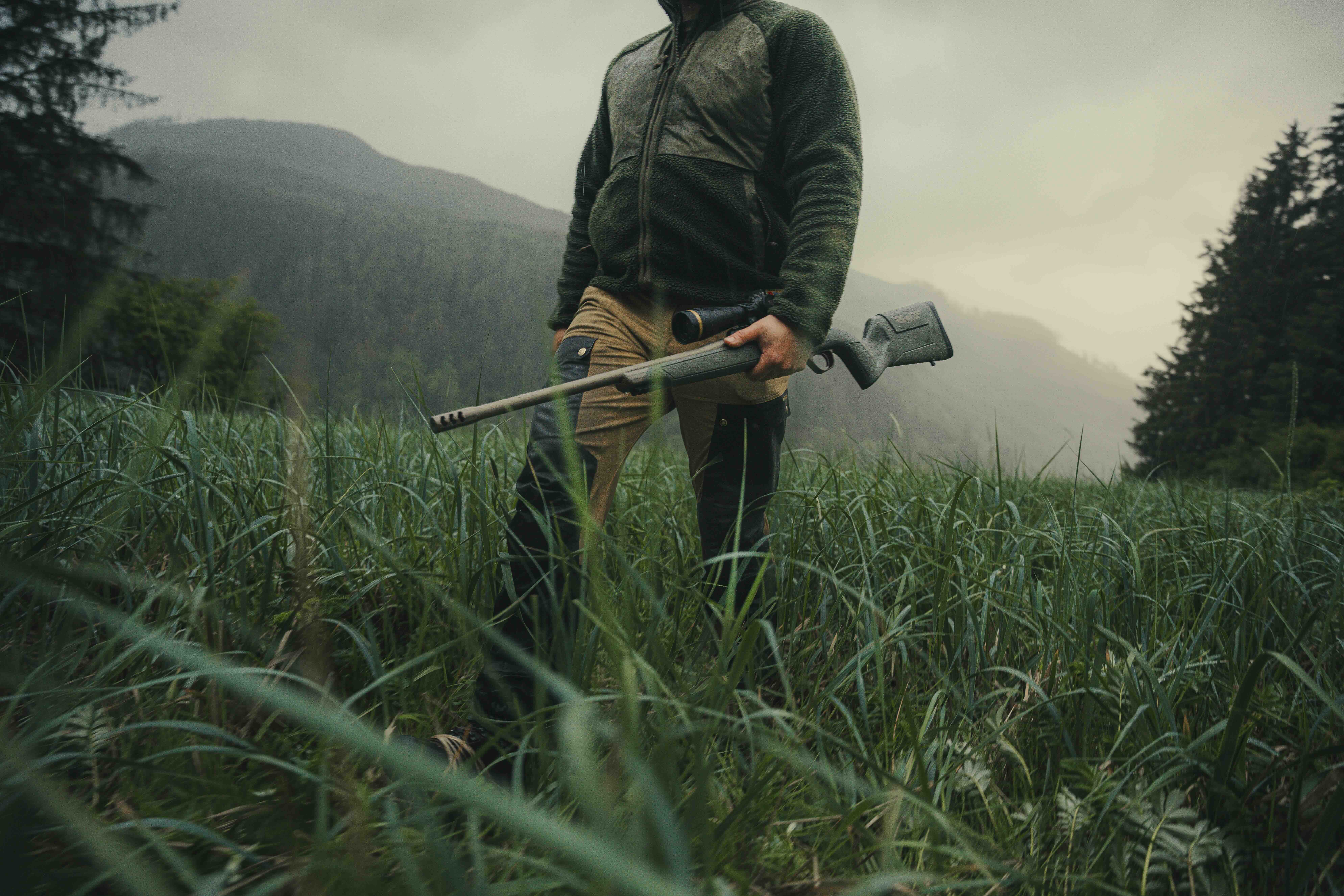 Hunter carrying a Christensen Arms Evoke hunting rifle through wet mountain terrain