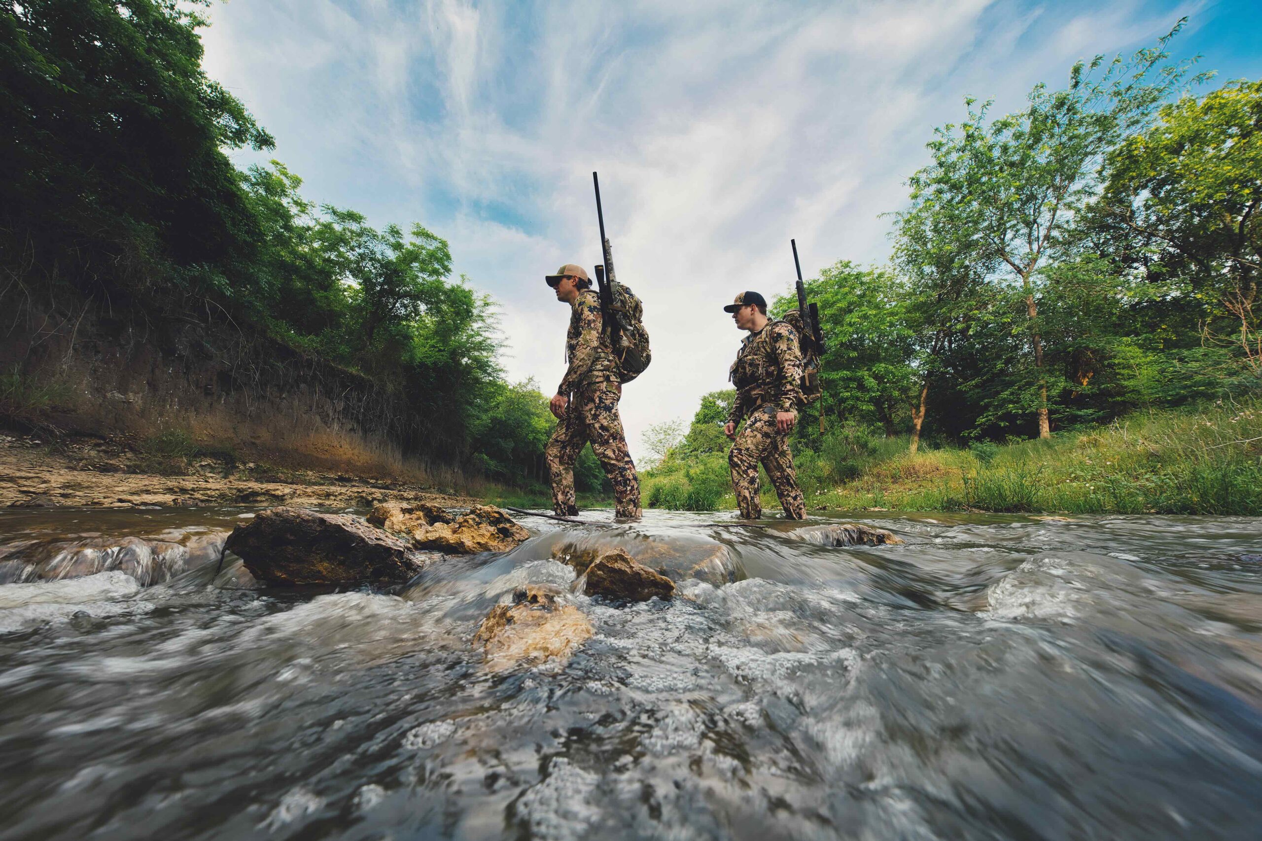 Hunters carrying rifles while crossing a creek