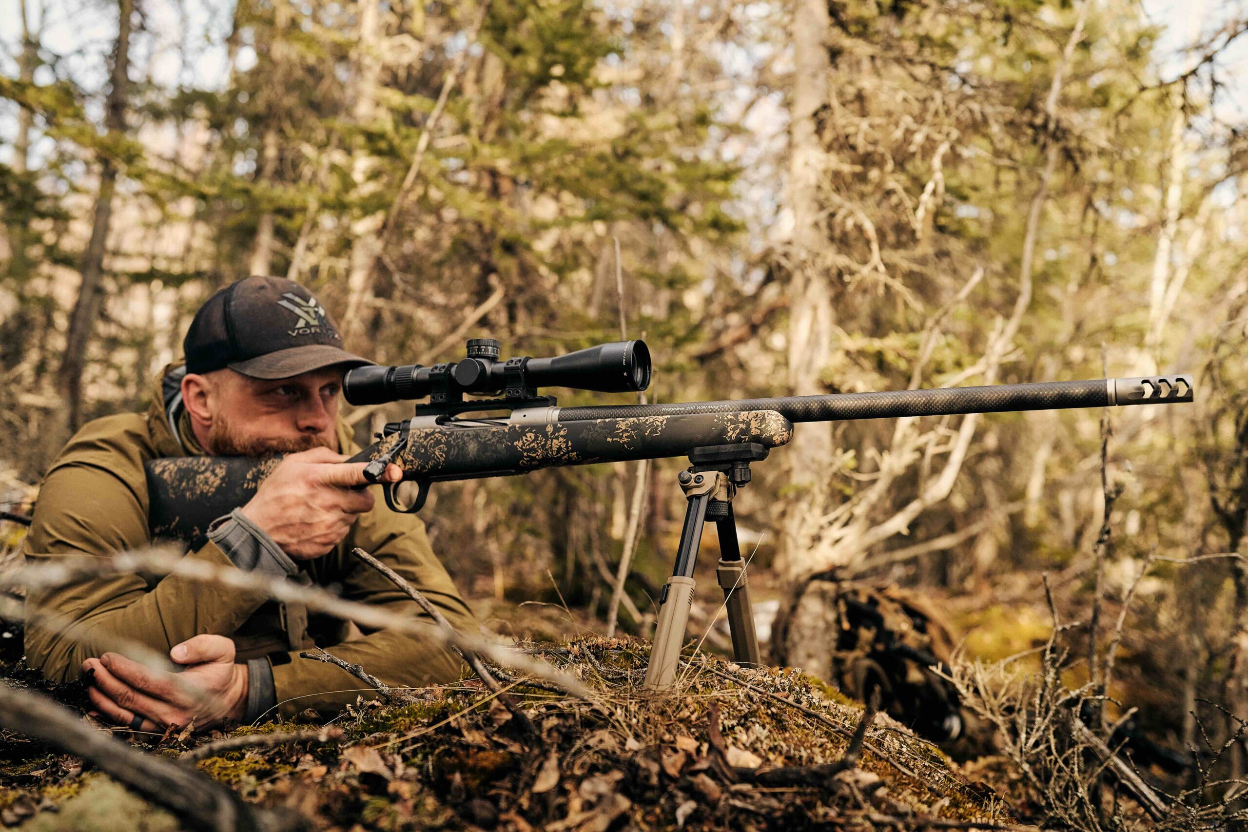Hunter behind a scoped Christensen Arms rifle supported on a tripod in the field