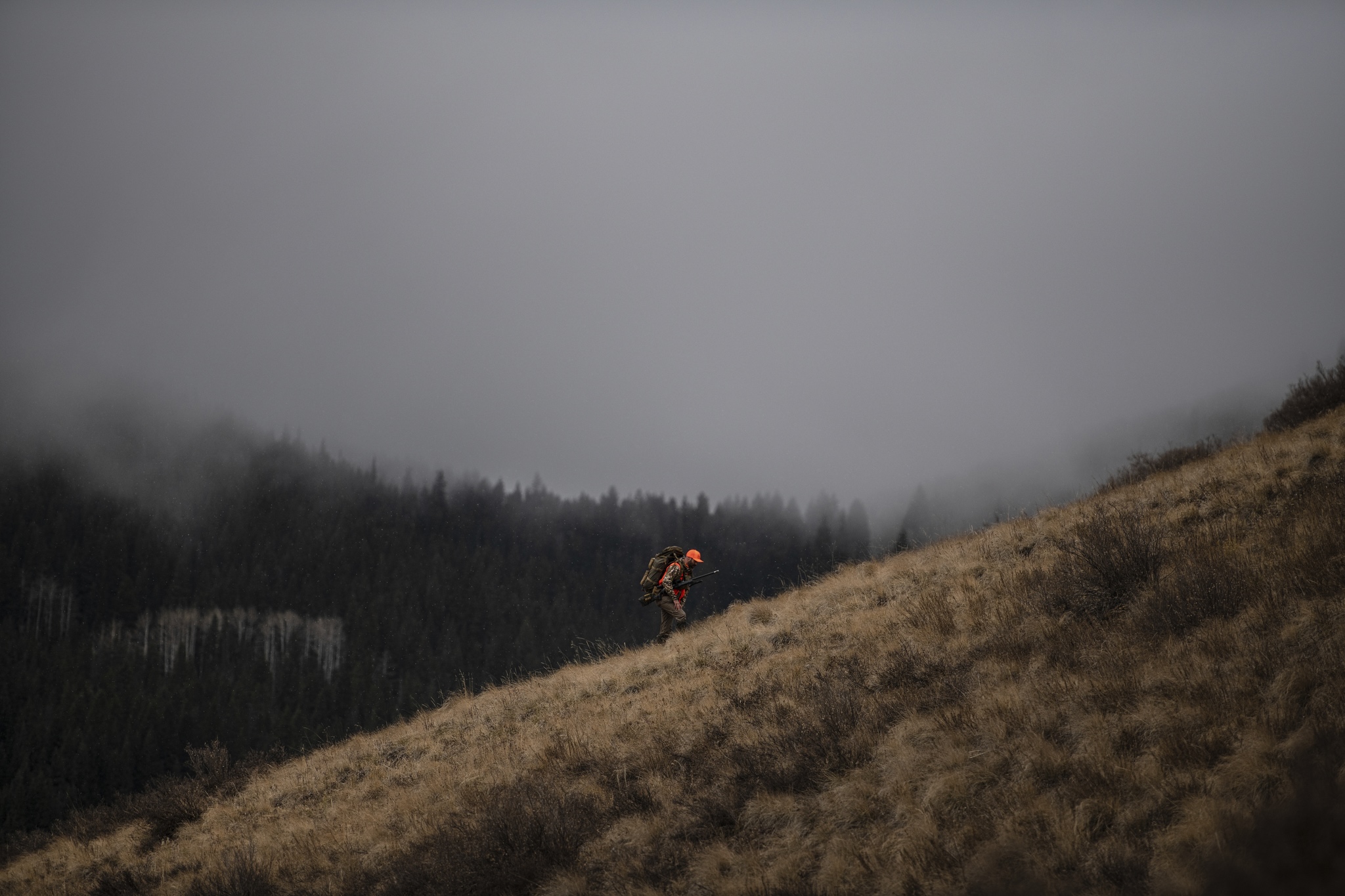 Hunter climbing a cloudy hillside with a loaded pack